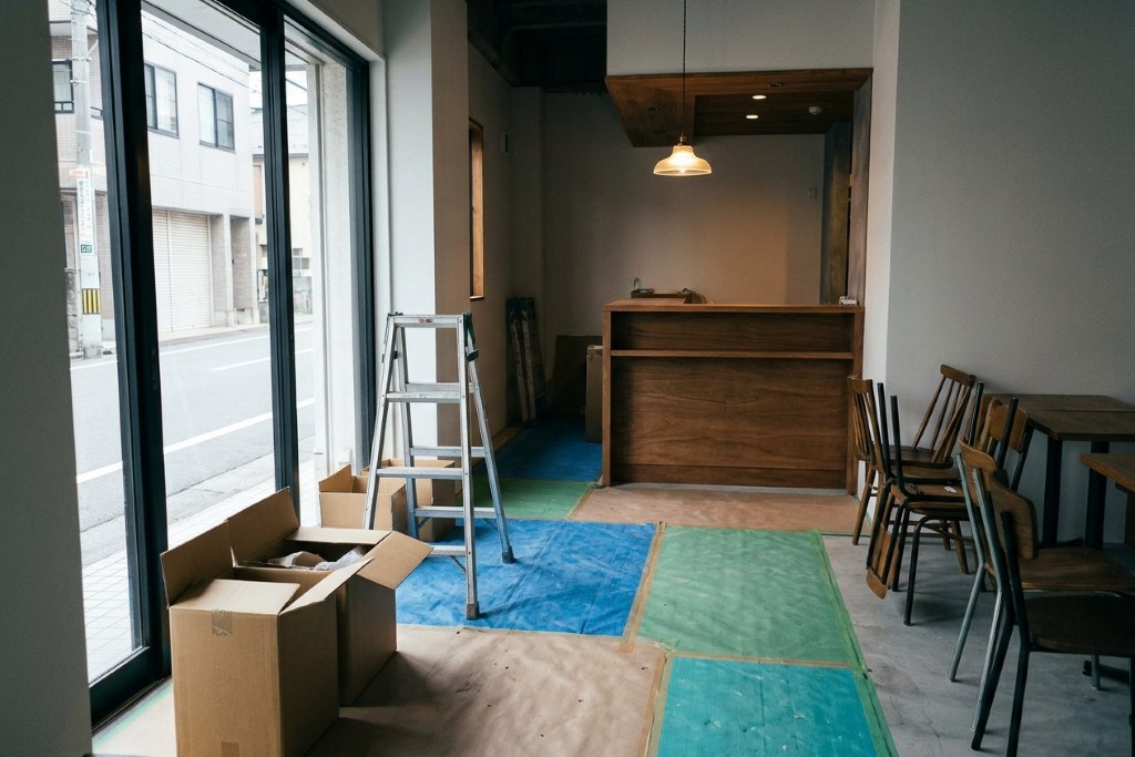 工事の仕上げ段階にある、木の造作カウンターとペンダント照明のある小さなカフェの店内